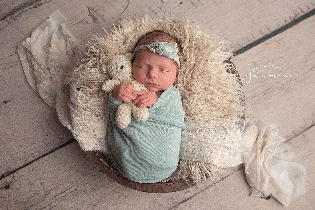 Baby girl wrapped in light blue in a prop holding a teddy