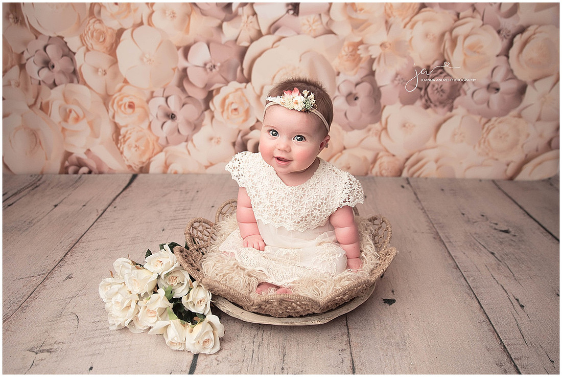 Six MOnth Baby Girl in Neutral tone dress sitting in a basket with flower backdrop