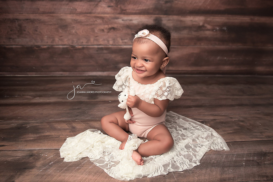 Baby sitting up with pink romper and lace