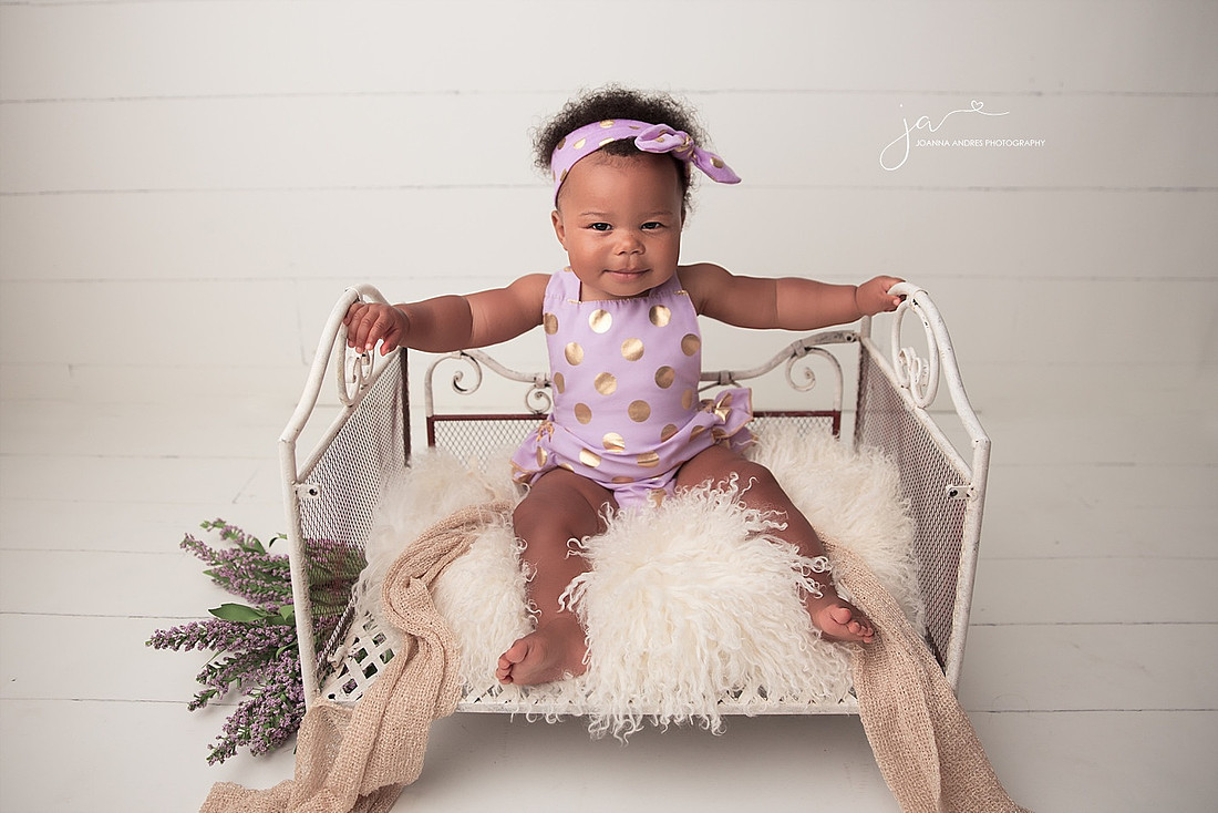 Baby girl in a white bed wearing purple with gold polka dots