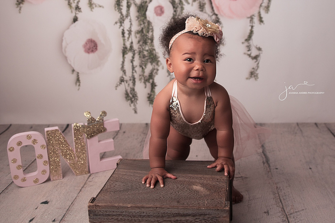 Baby girl leaning on a bench smiling for her one year photos